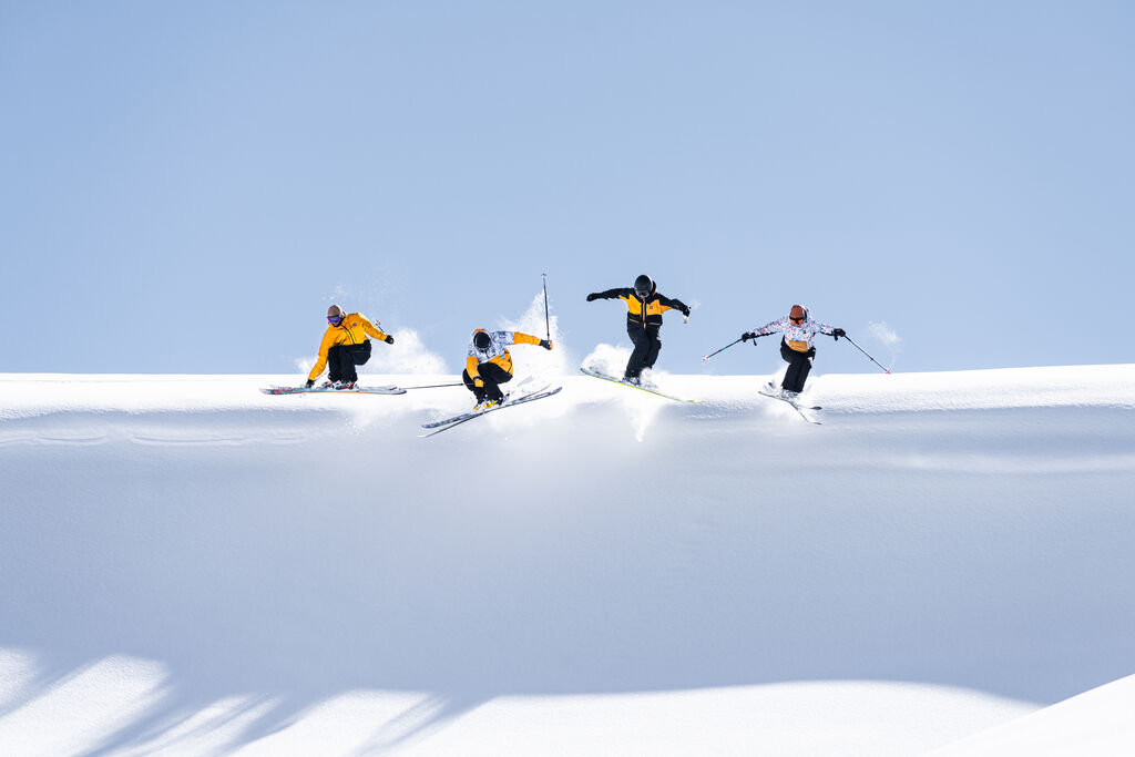 Four skiers in yellow outfits jumping off a hill at the same time